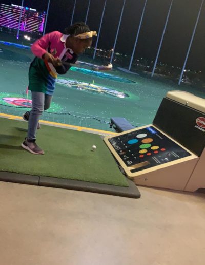 A girl swinging her golf club at the ball