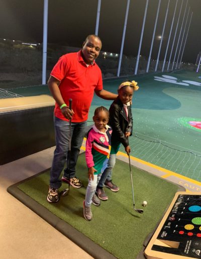 Two girls learning to play golf club with the help of an adult